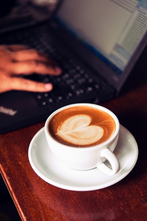 Businessman is working with laptop, holding a mobile phone in coffe shop and drinking coffe.の写真素材