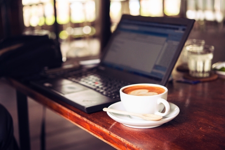 Businessman is working with laptop, holding a mobile phone in coffe shop and drinking coffe.の写真素材