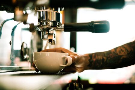 Coffee machine making coffee holded by tattooed barista armの写真素材
