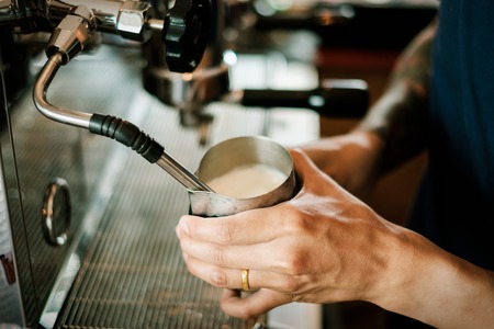 Coffee machine making coffee holded by tattooed barista armの写真素材