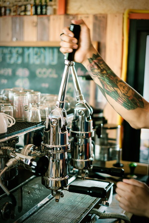 Coffee machine making coffee holded by tattooed barista armの写真素材