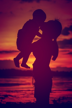 Silhouettes mother carries her son ,is background beautiful
 sunset on the lake.の写真素材