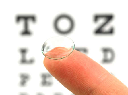 Contact lens on finger and snellen eye chart. The eye test chart is shown blurred in the background.の写真素材