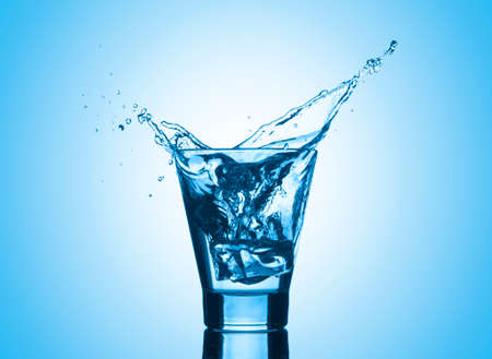 Water with splash and ice on blue background. Mineral water with ice in a glass.の写真素材