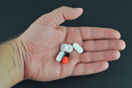 Pills in hand on dark grey background. Concept of Taking Your Medication.