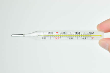 Thermometer in a hand on grey background. Thermometer showing the temperature of a healthy man. 36.6...