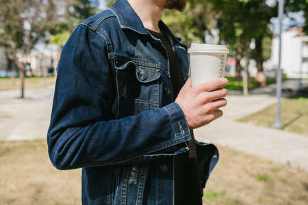 Young man wearing blue jean jacket leaning to a decorative stone in a park. Looking to phone scrolling, messaging or watching video.の写真素材