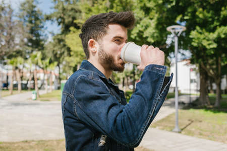 Walking, young man is walking in a green park with his hands in his pockets, a handsome adult wearing a denim jacket, nice weather and springの写真素材