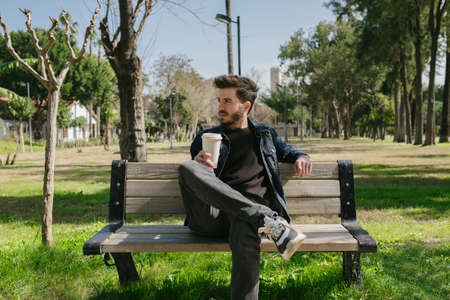 Young man wearing jeans jacket walking man stand step on the footpath trying shoelace shoes getting...