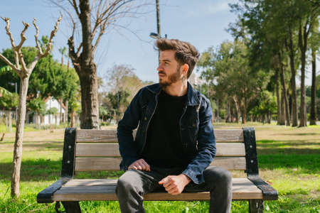 Young man wearing jeans jacket walking man stand step on the footpath trying shoelace shoes getting...
