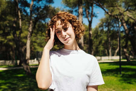 Happy young redhead woman wearing white tees holding a phone while looking away. Smiling woman using phone at outside. Selective focus on phone.の写真素材