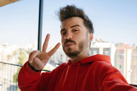 Young man wearing red hoodie holding smartphone with blank white screen and credit card or debit...