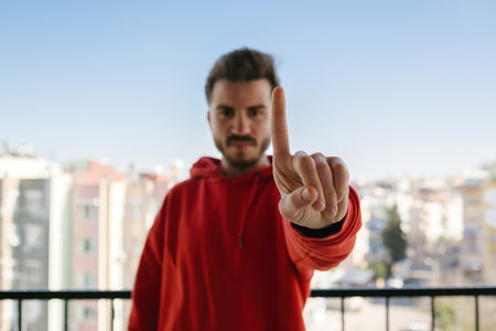 Young man wearing red hoodie holding smartphone with blank white screen and credit card or debit...