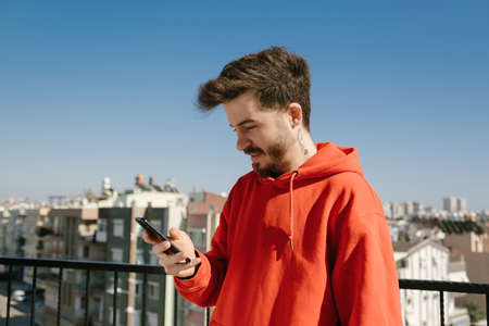 Young happy man wearing red hoodie excited cheerful joyful delightful curious guy sending and...