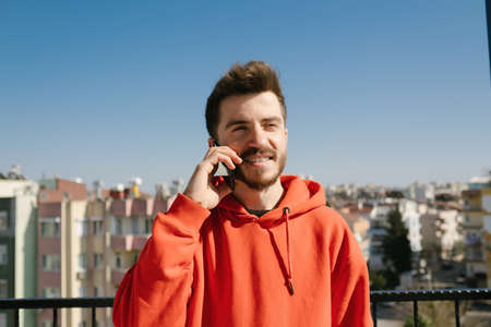 Young happy man wearing red hoodie excited cheerful joyful delightful curious guy sending and...