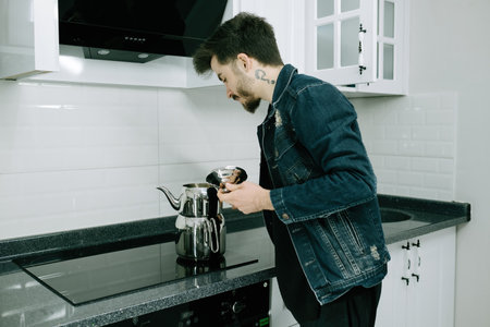 Kitchen, young man using kettle on electric stove, tea making and brewingの写真素材