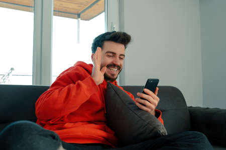 Facetime, the young man is video chatting with his friend and waving to him, young adult sitting on...
