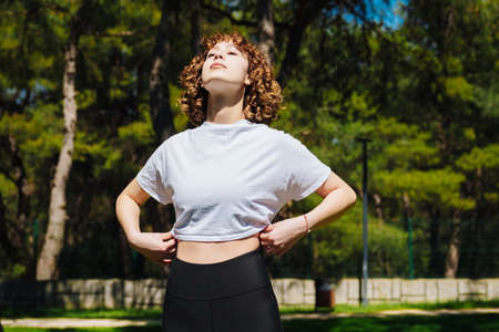 Redhead woman breathing fresh air in a green city park, outdoors. Enjoying stress free mindful...