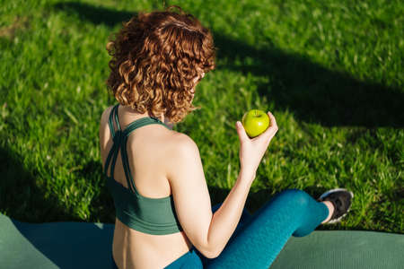 Young redhead woman wearing white tee using her smart phone while standing on a city park, outdoors. Watching video or messaging with friends or scrolling on social media.の写真素材