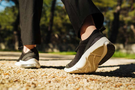 Woman walking in the park, outdoors. Taking a step. New life concept. Sportswoman exercising outdoors. Back view, selective focus on sneakers.の写真素材