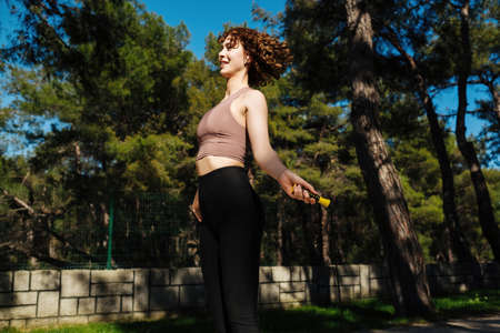 Fitness redhead female doing skipping workout outdoors. Portrait of fit young woman with jump rope...