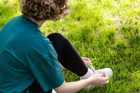 Cute caucasian woman wearing green t-shirt standing on city park, outdoor tying lace running shoes...