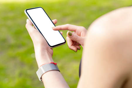 Young caucasian woman wearing sports bra standing on city park, outdoors hands holding phone with mockup white blank display, empty screen for social media. Mobile app tech concept.の写真素材