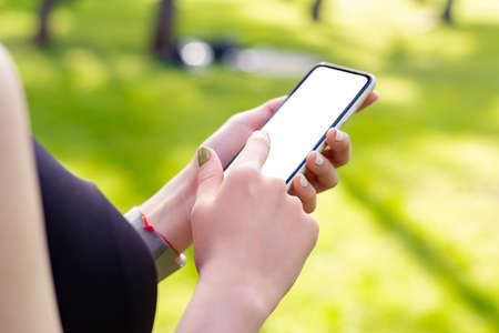 Redhead sportive woman wearing black sports bra standing on city park, outdoors hands holding phone with mockup white blank display, empty screen for social media. Mobile app tech concept.の写真素材