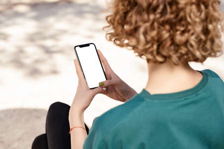 Beautiful redhead woman wearing sportive clothes standing on city park, outdoor holding phone...