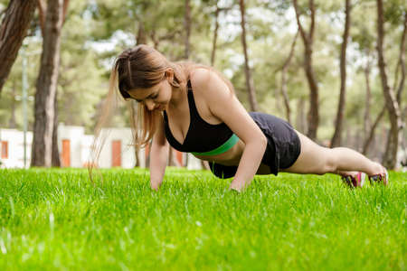 Young beautiful woman wearing sportive clothes on city park, outdoors. Confident girl doing push up...