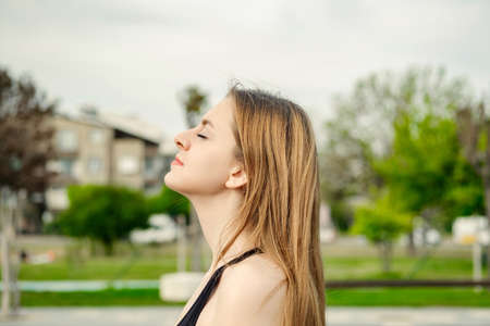 Brunette sportive woman wearing black sports bra standing on city park, outdoors relaxing with eyes closed, feeling alive, breathing, dreaming.の写真素材