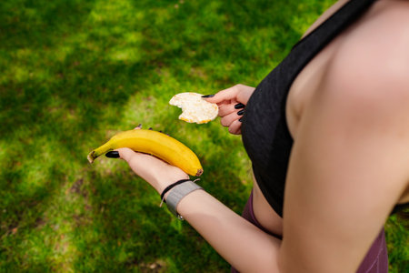 Young beautiful woman wearing sportive clothes on city park, outdoors holding a banana and rice cracker. Outdoor sport and healthy life concepts.の写真素材