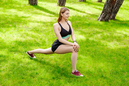 Happy sportive woman wearing sports bra standing on city park, outdoors doing stretching workout....