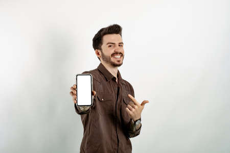 Cheerful young man wearing brown shirt posing isolated over white background showing to camera and...