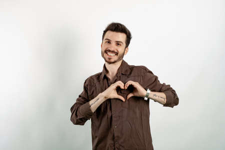 Happy casual man wearing casual clothes posing isolated over white background showing heart figure with fingers. Smiling in love doing heart symbol shape with hands. romantic concept.の写真素材