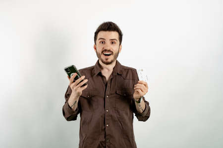 Caucasian man wearing brown shirt posing isolated over white background holding credit or debit card and smartphone in his hands, free space.の写真素材