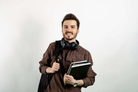 Cheerful caucasian man wearing brown shirt posing isolated over white background student with books and backpack and looking at the camera. High school university college concept.の写真素材
