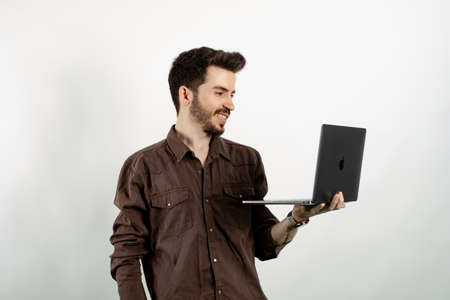 Happy young man wearing shirt posing isolated over white background standing and using laptop pc computer smiling with a happy and cool smile on face. Showing teeth.の写真素材