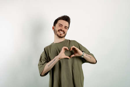 Cheerful caucasian man wearing casual clothes posing isolated over white background showing heart figure with fingers. Smiling in love doing heart symbol shape with hands. romantic concept.の写真素材