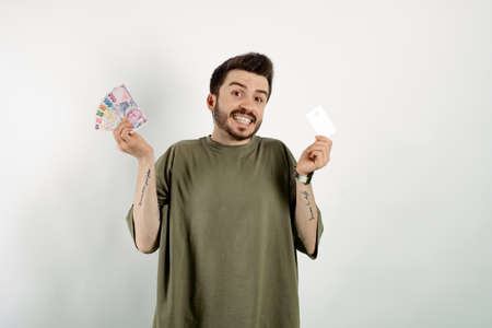 Happy casual man wearing t-shirt posing isolated over white background holding credit card and...