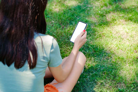 Young caucasian woman wearing tee standing on city park, outdoors hands holding phone touching...