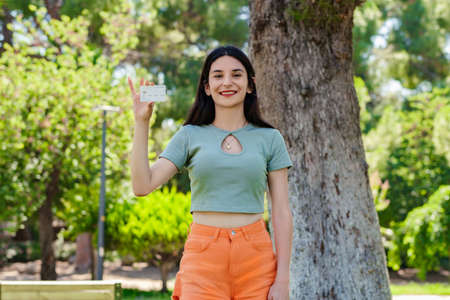 Cute caucasian woman wearing turquoise tee on city park, outdoors showing his plastic credit or debit card with hands. Shopping and finance concept.の写真素材