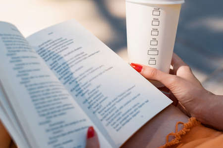 Young beautiful woman wearing turquoise tee on city park, outdoors reading book education studying learning knowledge and holding a takeaway coffee.の写真素材