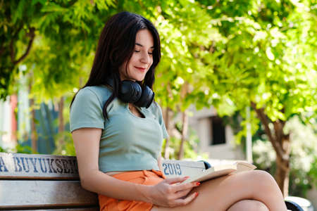 Young woman smiling confident wearing turquoise tee and orange short on city park, outdoors sitting...