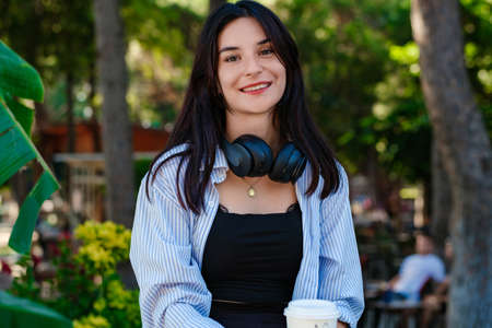 Portrait of cheerful woman wearing striped shirt standing on city park, outdoors looking at camera...