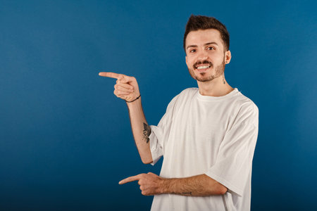 Happy casual man wearing t-shirt posing isolated over blue background smiling and looking at the...