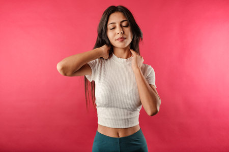 Young beautiful woman wearing ribbed crop isolated over red background with severe neck pain massages neck with eyes closed and tries to relax.の写真素材
