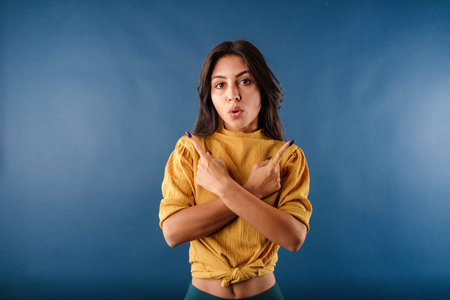 Young beautiful woman wearing yellow top isolated over blue background crosses arms and points...