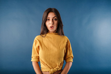 Portrait of young brunette woman isolated over blue background shocked woman looking at the camera...