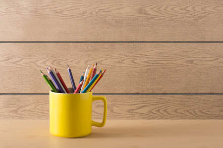 Yellow cup with colour pencil on wood textureの写真素材